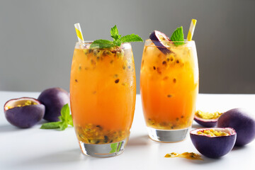 Tasty passion fruit drink with mint in glasses and fresh fruits on light table against gray background