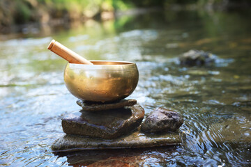 Tibetan singing bowl with mallet on stone in river