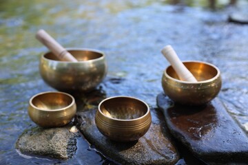 Tibetan singing bowls with mallets on stones in river, closeup