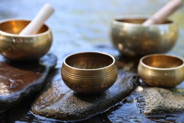 Tibetan singing bowls with mallets on stones in river, closeup