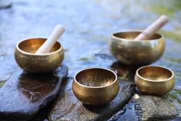 Tibetan singing bowls with mallets on stones in river, closeup