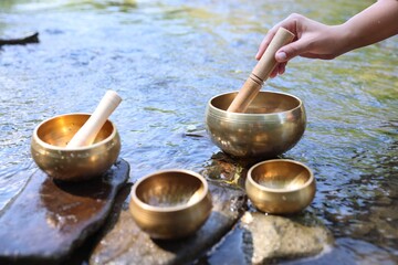 Woman with singing bowls by river, closeup