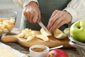 Making delicious apple strudel. Woman cutting fresh fruit at wooden table in kitchen, closeup