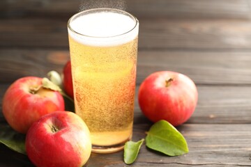 Delicious cider in glass, apples and green leaves on wooden table, closeup