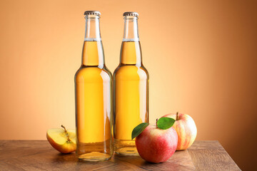 Delicious cider in glass bottles and apples on wooden table against orange gradient background
