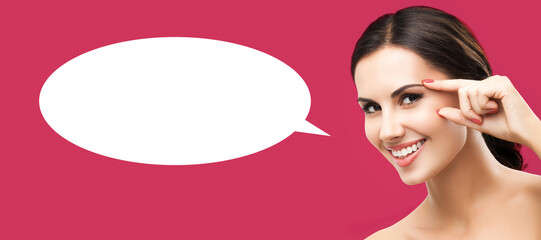 Skin care beauty concept. Portrait of happy smiling cute brunette woman pointing showing brow or eye, touching skin, isolate red background with white empty mockup speech bubble. Banner image