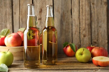 Delicious cider in glass bottles and apples on wooden table. Space for text