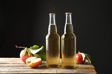 Delicious cider in glass bottles and apples on wooden table against dark gray background