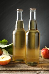 Delicious cider in glass bottles and apples on wooden table against dark gray background