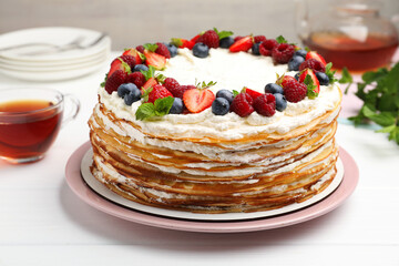 Delicious crepe cake with fresh berries and tea on white wooden table, closeup