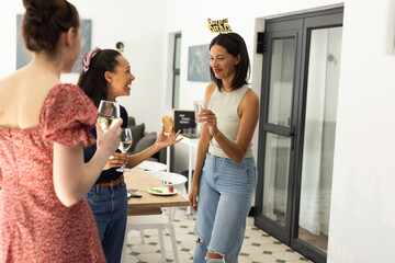 Laughing and chatting, three young women enjoy drinks at home