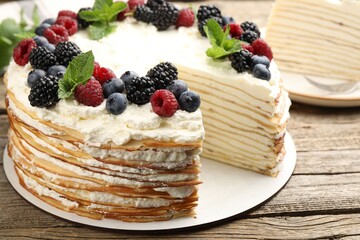 Tasty crepe cake with berries and mint on wooden table, closeup