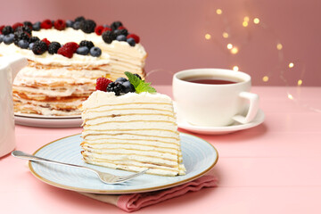 Piece of tasty crepe cake with berries served on pink wooden table against blurred lights, closeup