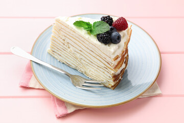Piece of tasty crepe cake with berries served on pink wooden table, closeup