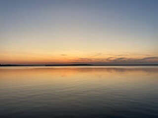 Sunset over calm water with soft sky reflections and distant structure — tranquil nature scene for visual serenity and contemplative themes