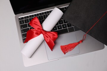 Graduation cap, laptop and diploma on light table, flat lay