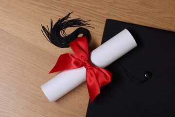 Graduation cap and diploma on wooden table, flat lay