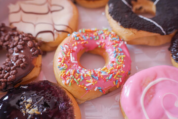 A person's hand takes a delicious donut from a box of twelve assorted pastries with colorful toppings.	