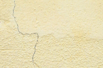 Obraz premium A close-up of a pale yellow wall reveals a rough surface and a dark vertical crack, symbolizing age, wear, and the need for renovation.