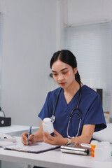Female doctor carefully checking medicine bottle and writing prescription in medical office