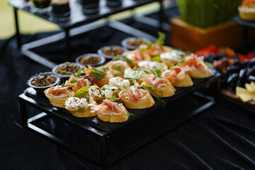 Bruschetta with prosciutto, mozzarella, and greens served on a black stand for buffet.
