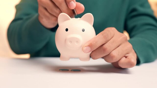 A person puts a coin into a piggy bank, but the coin falls straight through the bottom, symbolizing inability to save money, financial leakage, insecurity, and the frustration of unachieved goals.

