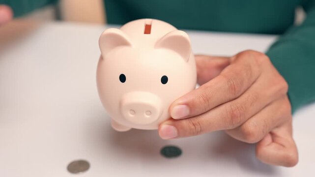 An office worker puts coins into a piggy bank, but they fall straight out the bottom, symbolizing failed saving efforts, financial setbacks, instability, and the frustration of unmet financial goals.
