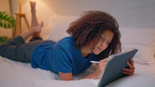 Attractive Latina woman lying on bed at night using digital tablet. 