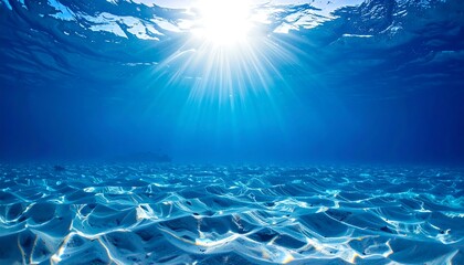 Sunlight streams from above underwater, illuminating sandy ocean floor. Blue water with rays