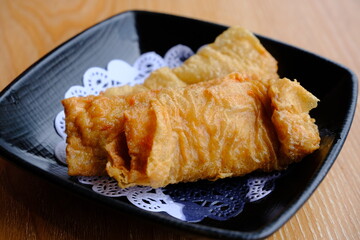 Crispy fried tofu skin rolls served on a black plate with paper doily, a popular Asian vegetarian snack or dim sum dish.  
