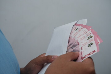 Close-up of hands holding an envelope containing Indonesian rupiah banknotes, representing salary...