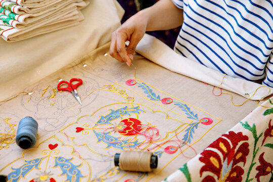 In Tashkent, Uzbekistan, an artisan carefully hand-embroiders a vibrant floral pattern, surrounded by traditional Uzbek textiles. A glimpse into Uzbek craftsmanship heritage.