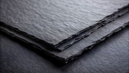 Dark gray slate sheets with textured rough edges stacked close up