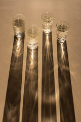 Four glasses of sparkling water casting long shadows on a beige background, light and shadows art