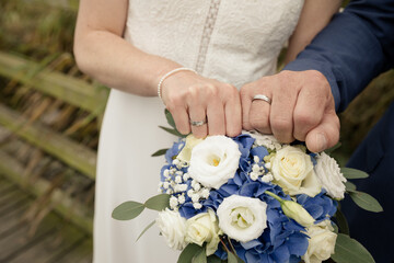 Braut und Br&auml;utigam pr&auml;sentieren Eheringe und ihr Hochzeitsoutfit
