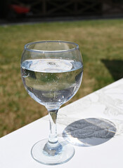 Clear glass filled with sparkling water resting on a white table in a sunny outdoor setting often enjoyed in warm weather