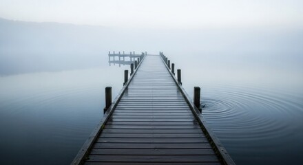 Naklejka premium A wooden pier stretches over still water, disappearing into a hazy, misty atmosphere. Gentle ripples emanate