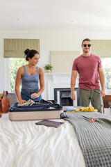 Couple packing suitcase in bedroom, preparing for travel with excitement