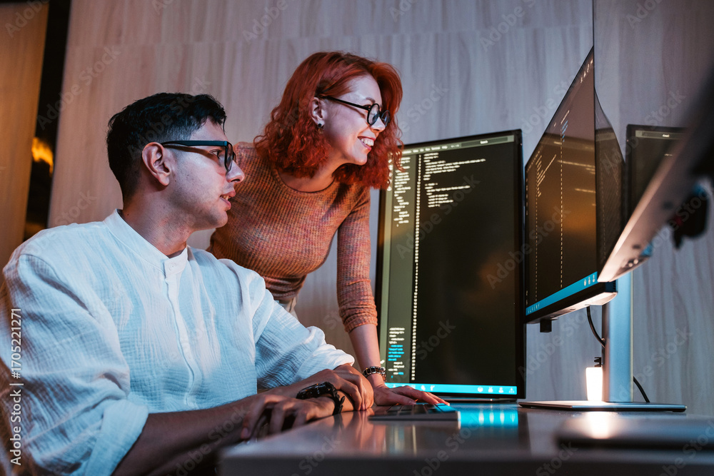 Poster two colleagues collaborate at dual monitors in a modern office, reviewing code on screens and discus