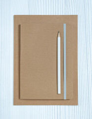 Minimalist sustainable stationery set with kraft notebooks and pencil on white wooden background.
