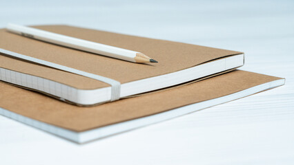 Minimalist sustainable stationery set with kraft notebooks and pencil on white wooden background.