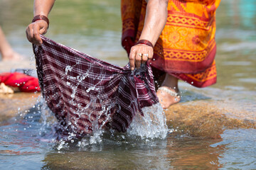 Indian woman washing clothes at Tungabhadra river, Hampi, colorful fabrics, traditional bangles on arm, lifestyle and culture of India