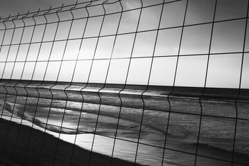 Black and white sunset view of the ocean through a wire fence
