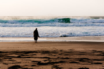 Woman standing barefoot on the beach looking at ocean waves in Portugal