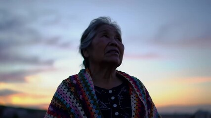 Portrait of a serene senior woman in a colorful handmade shawl contemplating the beautiful twilight sky