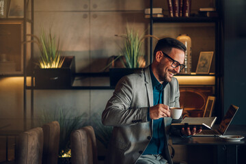 Happy businessman drinking coffee and working on laptop in cafe