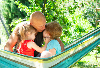 Cheerful family relaxing outdoors in the park at summer day, grandfather kissing and hugging grandchildren 