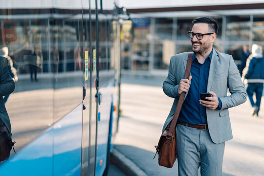 Businessman walking near bus holding smartphone and smiling
