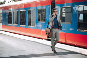 Businessman walking and talking on smartphone at train station