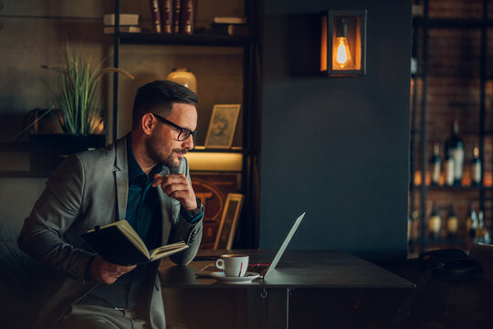 Businessman working on laptop and reading notes in cafe